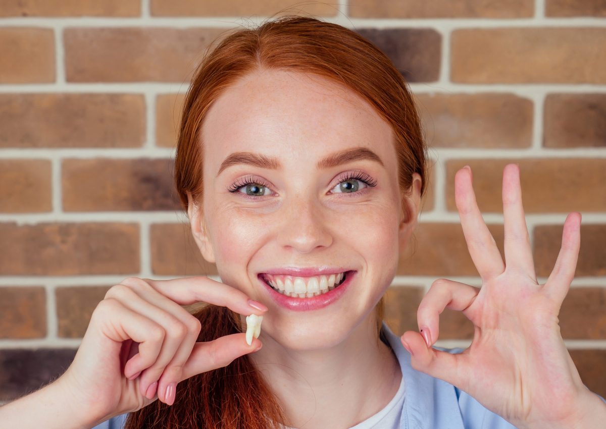 redhaired ginger female with snow-white smile holding white wisdom tooth after surgery removal of a tooth